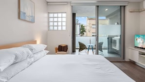A hotel room with a bed, a chair, a small table, a TV, and a balcony with a view of the city.