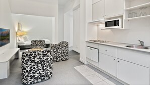 A modern kitchen with white cabinets, a microwave, and a sink. There is a dining area with a table and chairs. - Inner-City Studio – Walk to Everything! (Melbourne)