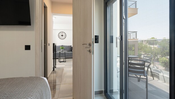 Una moderna camera d'hotel con un letto, una TV, un balcone con tavolo e sedie e vista sulla città.