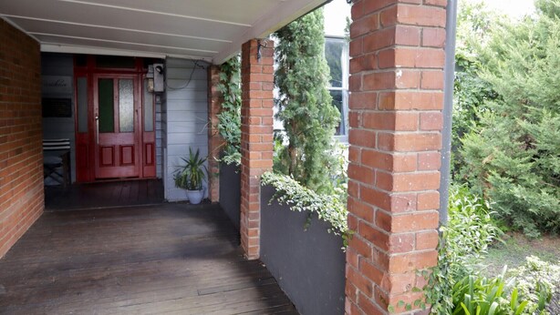 A covered porch with a red door, brick walls, and potted plants. - Towncottage Tenterfield Stay with Scenic Views (Tenterfield)