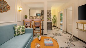 A living room with a sofa, a coffee table with books and candles, a dining area with chairs and a table, and a kitchen in the background. - Staymaster Veridian 2BR - Standard (Calangute)