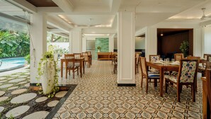 A spacious dining area with a patterned floor, wooden furniture, and a view of a pool. - Staymaster Veridian 2BR - Standard (Calangute)