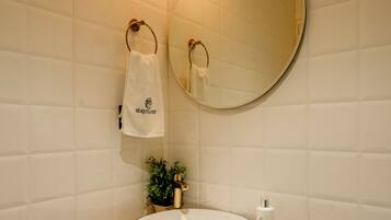 Ein Badezimmer mit rundem Spiegel, Waschbecken mit Holzablage, Handtuch auf einem Handtuchhalter und Toilettenpapierhalter.