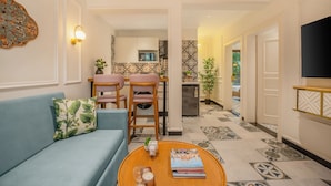 A living room with a sofa, a coffee table with books and candles, a dining area with chairs and a table, and a kitchen in the background. - Staymaster Veridian 2BR - Standard (Calangute)