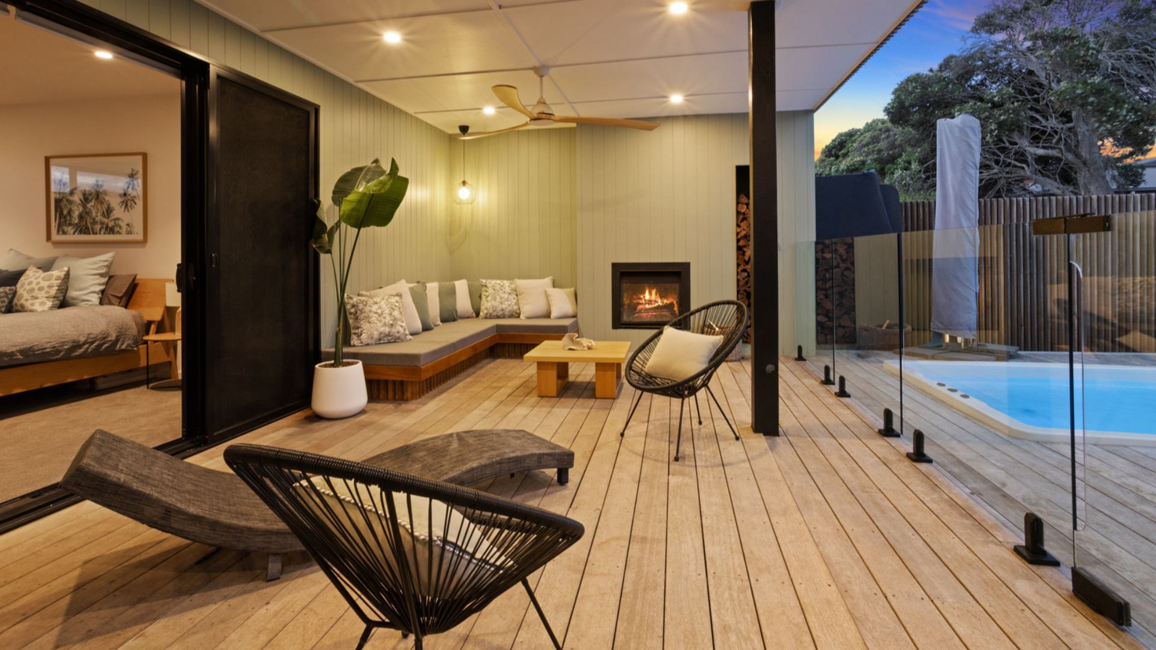 A modern outdoor living area with a wooden deck, seating, a fire feature, and a pool.