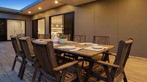 An outdoor dining area with a wooden table and chairs, a potted plant, and a view of the interior. - Salty Sixteen Rye Retreat with Pool (Rye)