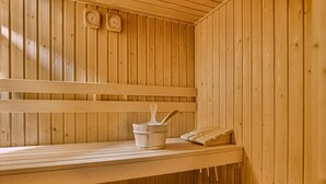 A wooden sauna with benches, a bucket, and two wall clocks. - 6-person Comfort Bungalow With Sauna (Kootwijk)
