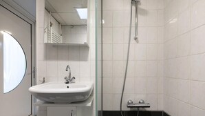 A bathroom with a white sink, a mirror, a shower, and a black-tiled shower area. - 6-person Comfort Bungalow With Sauna (Kootwijk)