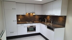 A modern kitchen with white cabinetry, a gas stove, a built-in oven, a dishwasher, and a black countertop. - 6-person Comfort Bungalow With Sauna (Kootwijk)