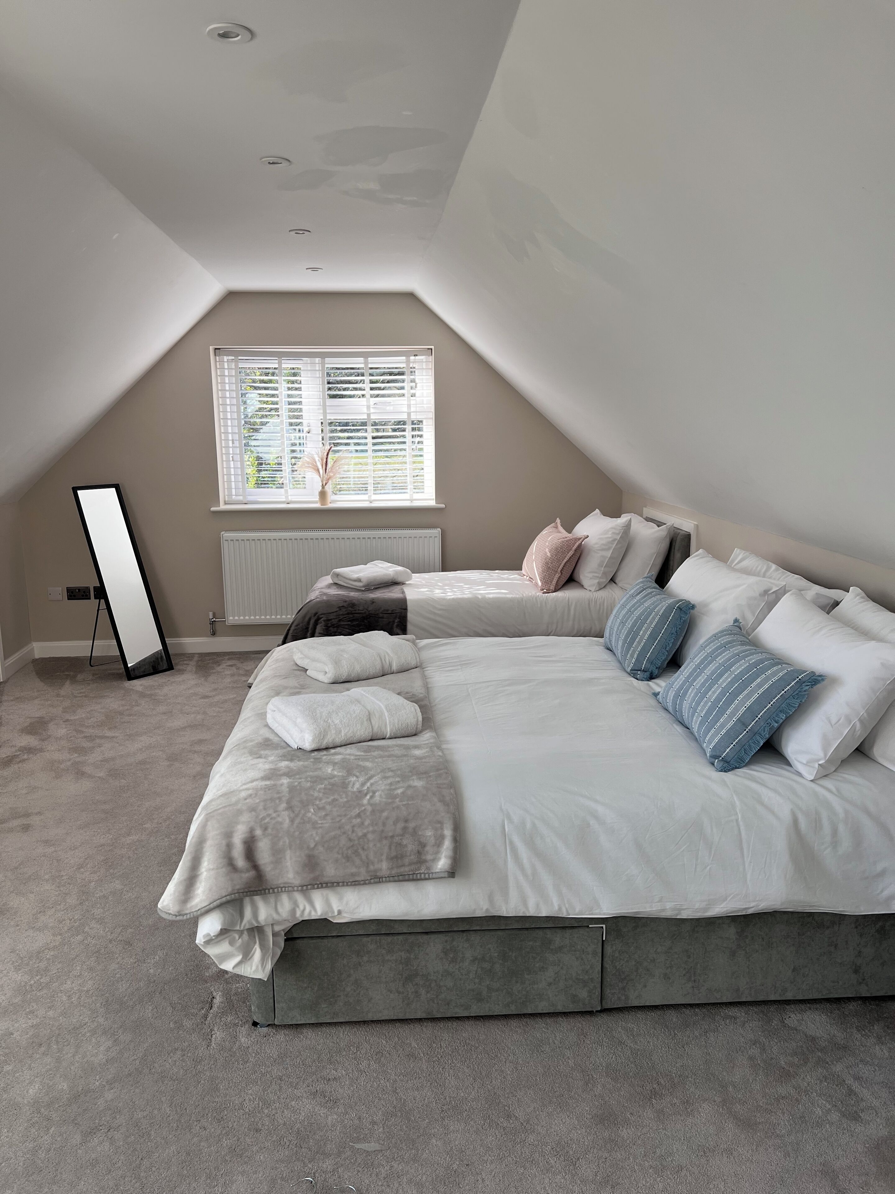 A bedroom with a large bed, a radiator, a window with blinds, and a ceiling fan.