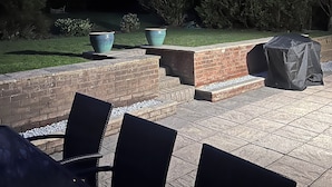 Un patio al aire libre con escalones de ladrillo, asientos exteriores e iluminación colgante.