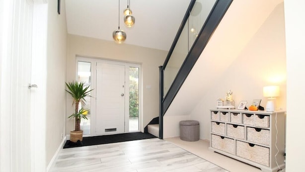Un interior moderno con una escalera, una planta en maceta, una puerta blanca y un mueble de almacenaje.