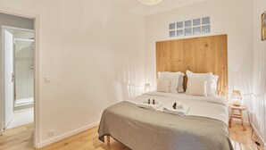 Ein Schlafzimmer mit hölzernem Kopfteil, einem Bett mit weißer Bettwäsche, einem Nachttisch mit Lampe und einem Fenster mit satinierten Glasfeldern.