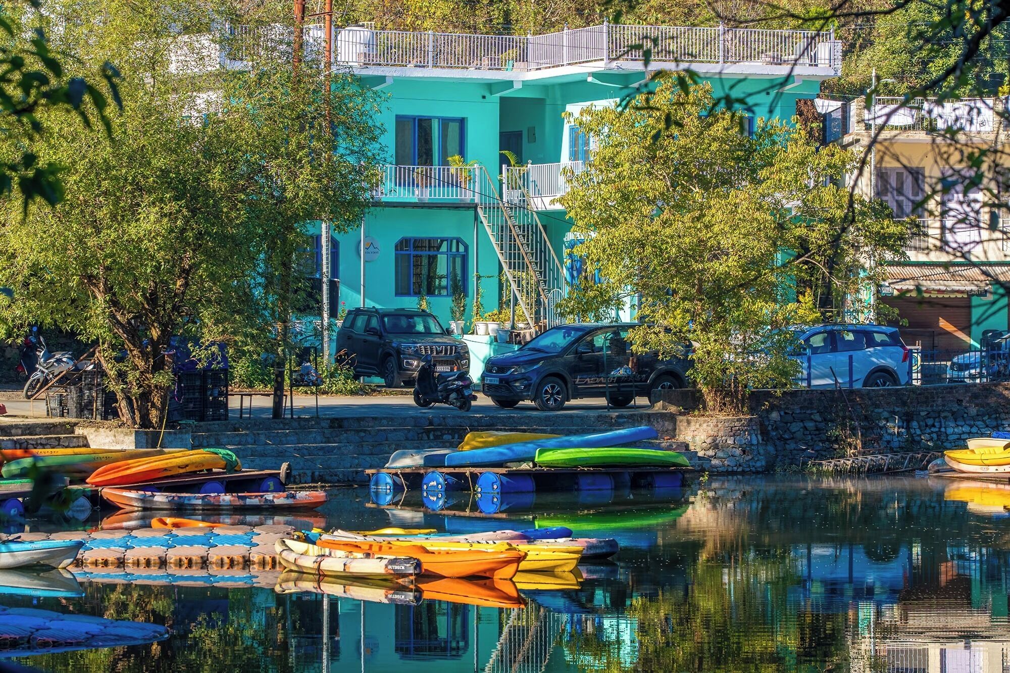 A waterfront property with boats, a building with balconies, and parked cars.