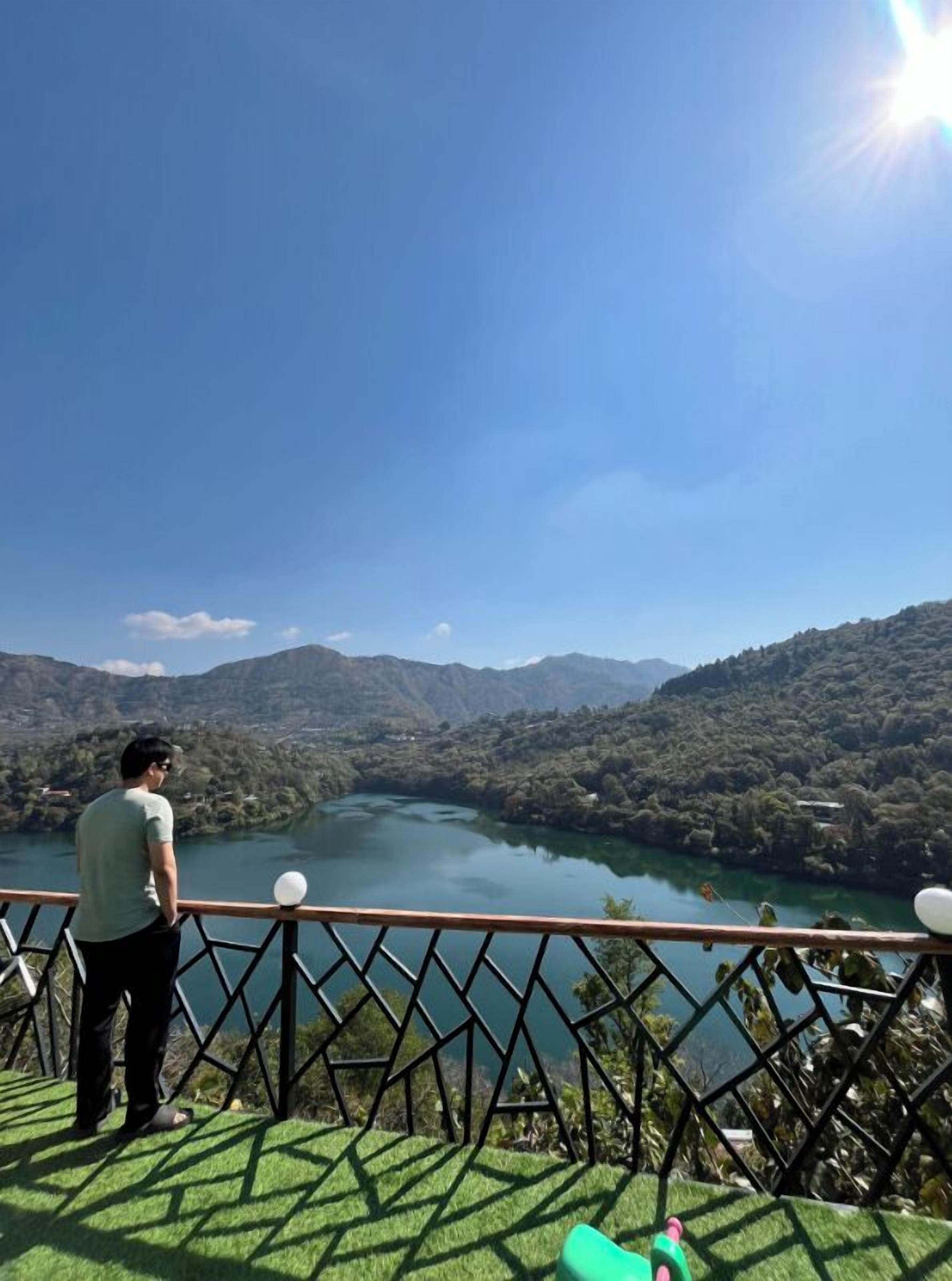 A person standing on a balcony overlooking a lake with mountains in the background.