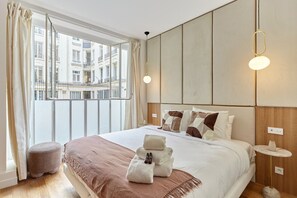 A hotel room with a large bed, a view of buildings through the window, and a small round table with a lamp. - Exceptional AC Apartment - Center of Paris (Paris)