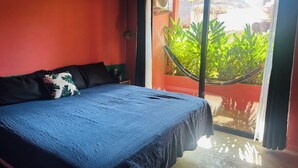Un dormitorio con una cama, una mesita de noche, un ventanal con vistas a la vegetación y una pared roja.