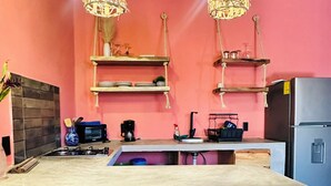 Una cocina con una isla central, taburetes de bar, lámparas de mimbre colgantes y un refrigerador.
