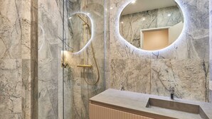 Une salle de bain moderne avec des murs en marbre, une douche en verre, un miroir rond et un meuble-lavabo en bois.