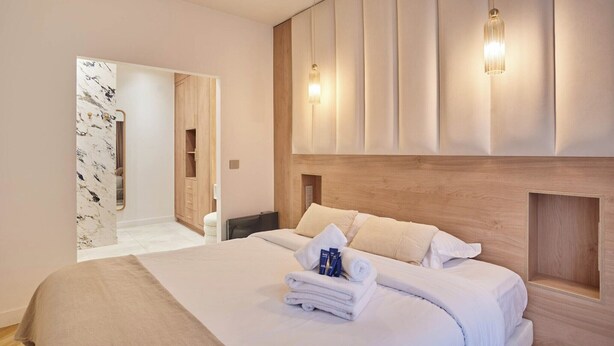 Une chambre d’hôtel moderne avec un grand lit, une tête de lit en bois et un miroir.