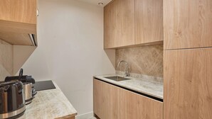 Une cuisine compacte avec des meubles en bois, un plan de travail en marbre, un évier et une bouilloire.