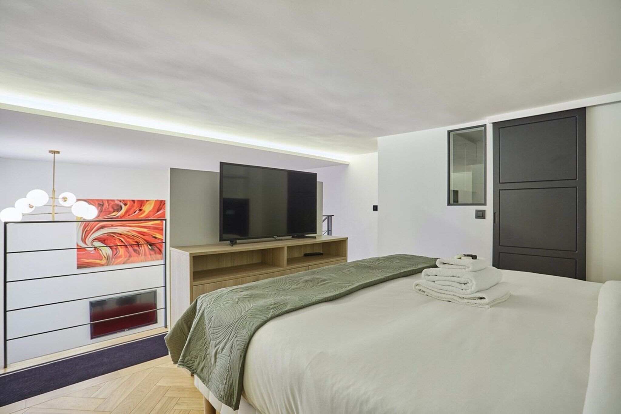 Une chambre d’hôtel moderne, équipée d’un lit, d’un téléviseur à écran plat, d’une commode en bois et d’un tableau au mur.