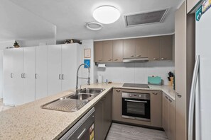 A modern kitchen with white and brown cabinets, stainless steel appliances, and a granite countertop. - Stylish Bowen Hills Studio Near City Centre (Bowen Hills)