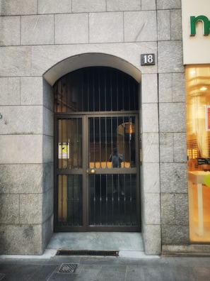 Ein Steinhaus mit einem schwarzen Metallgitter, einem Schild mit der Aufschrift '18' und einem Geschäft mit einer grünen Werbetafel.