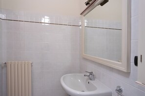 Ein Badezimmer mit weißen Fliesen, einem weißen Waschbecken, einem Spiegel und einem Handtuchhalter.