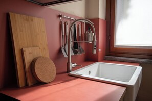 A modern kitchen with a white sink, stainless steel faucet, and a variety of utensils hanging on a rack. - The Haven Suite in Duomo (Milano)