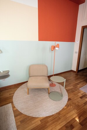 A room with a beige armchair, a small round table, a floor lamp, and a rug on a wooden floor. - The Haven Suite in Duomo (Milano)