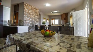 Un coin repas avec une table dressée pour deux personnes, un mur décoratif en pierre et une vue sur la cuisine.