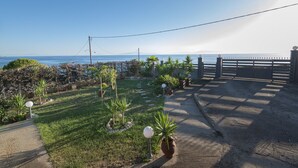 Un chemin pavé mène à une entrée fermée par un portail, d’où l’on peut admirer la mer.