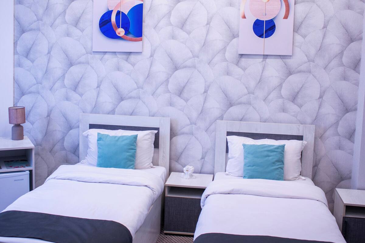 A hotel room with two beds, a textured wall, and artwork.