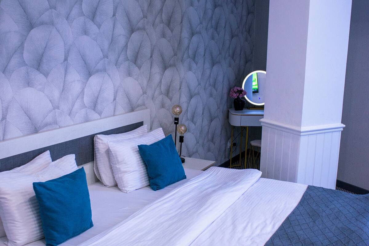 A bed with white and blue bedding, a textured wall behind it, and a small vanity with a mirror and a lamp.