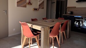 Ein zeitgemäßer Essbereich mit Holztisch und roten Stühlen, im Hintergrund eine Küche, und Sonnenlicht wirft Schatten auf den Boden.