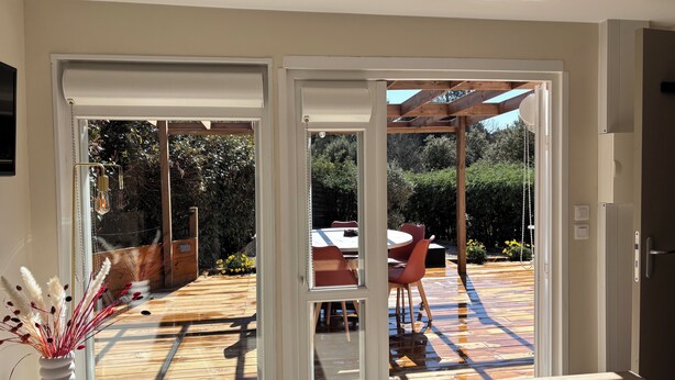 Ein Zimmer mit einer Schiebetür und Zugang zu einer Terrasse mit Holzdeck, einem Tisch und Stühlen.