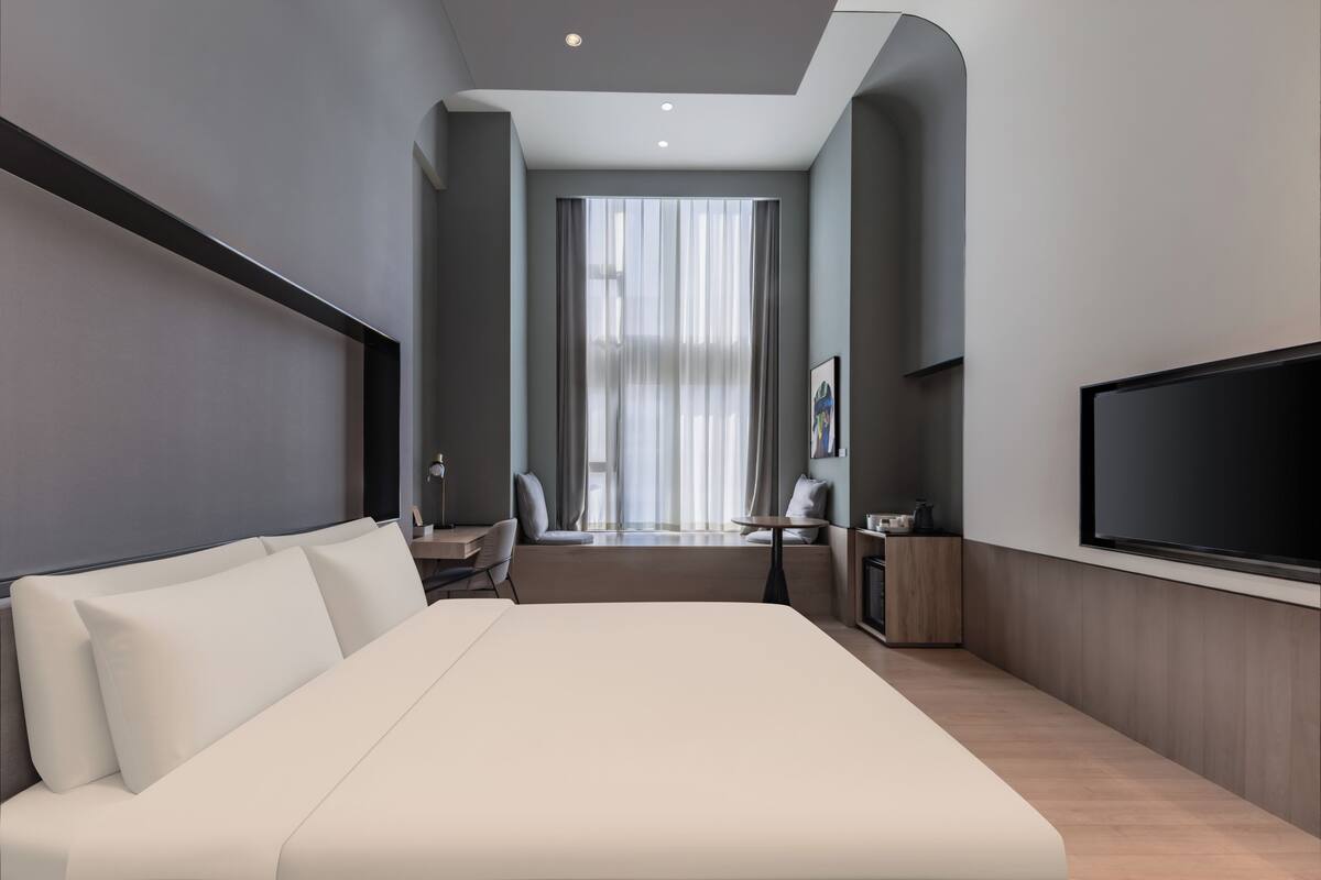 Een moderne hotelkamer met een groot bed, een bureau, een stoel, een televisie en een raam met gordijnen.
