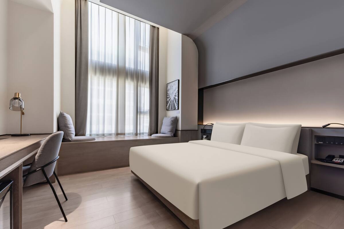 Een moderne hotelkamer met een bed, bureau, stoel en een raam met gordijnen.