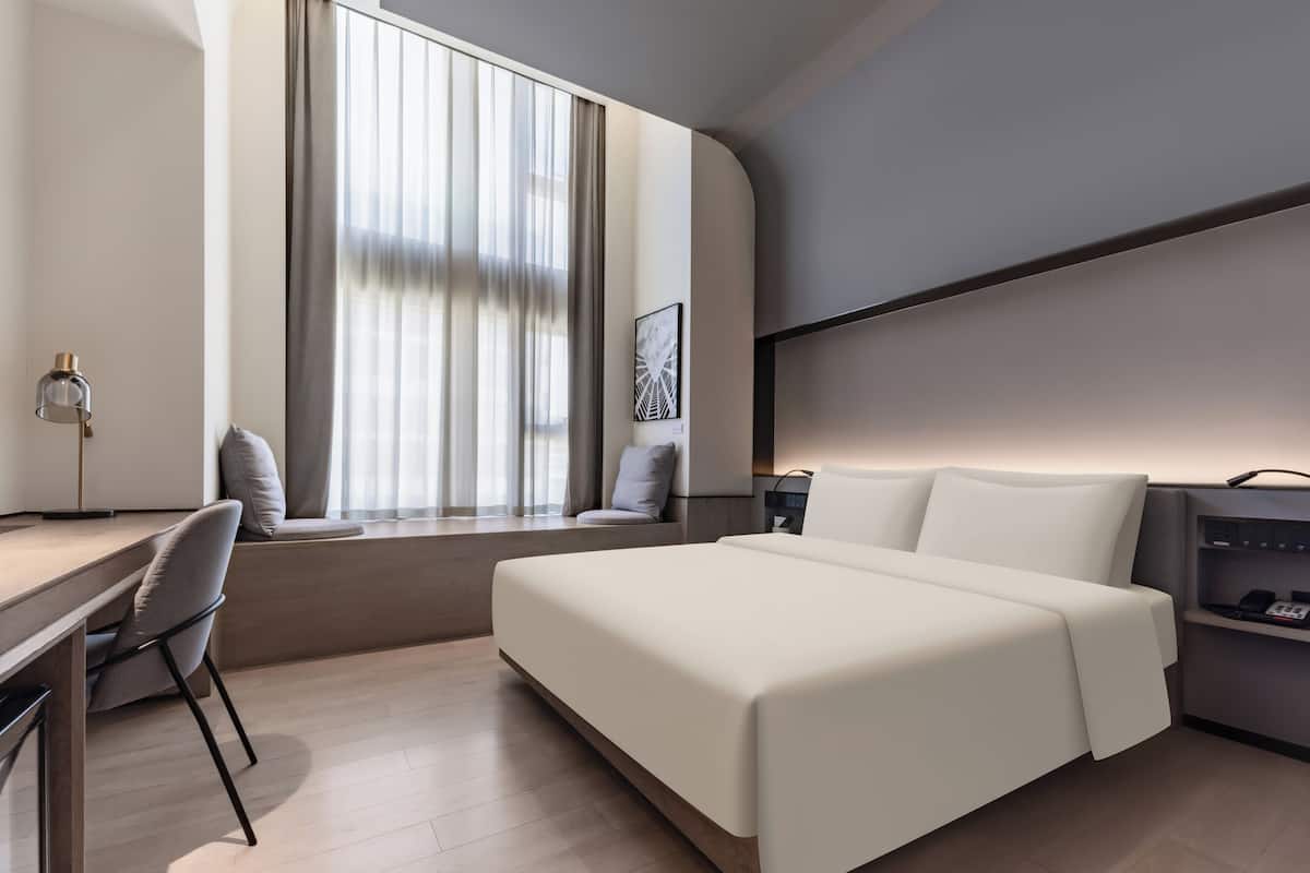 Une chambre d’hôtel moderne équipée d’un lit, d’un bureau, d’une chaise et d’une fenêtre avec des rideaux.