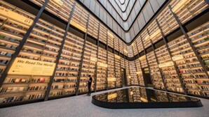 Une bibliothèque moderne où les étagères sont disposées en cercle, avec une table en verre au centre et une pancarte sur laquelle on peut lire : « Nous explorons le monde à travers la lecture. »