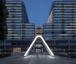 A modern hotel with a distinctive arched entrance, large windows, and a well-lit facade. - Atour S Hotel  Hongqiao Center Shanghai (Shanghai)