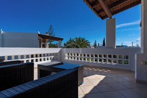 A rooftop terrace with wicker furniture, a pool, and a view of the surrounding landscape.