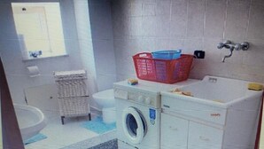Een wasruimte met een wasmachine, een droogrek en een rode mand.