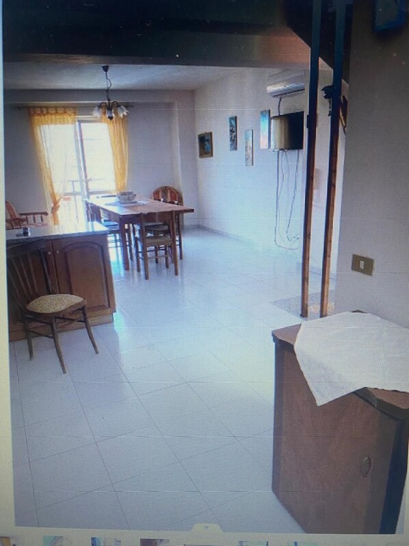 A room with a dining table, chairs, a window with curtains, and a wall-mounted television.