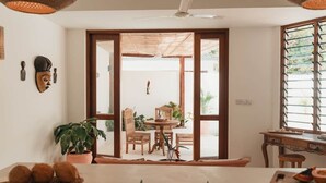 Una cocina con estufa a gas, una mesa de comedor con sillas, una planta en maceta y vistas al exterior a través de un ventanal.