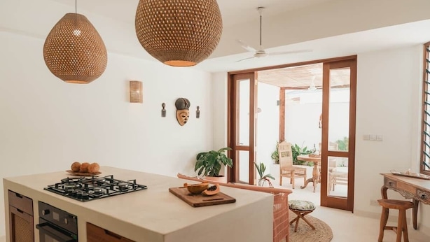 Una cocina moderna con una isla central, luces colgantes y vistas a un espacio exterior.