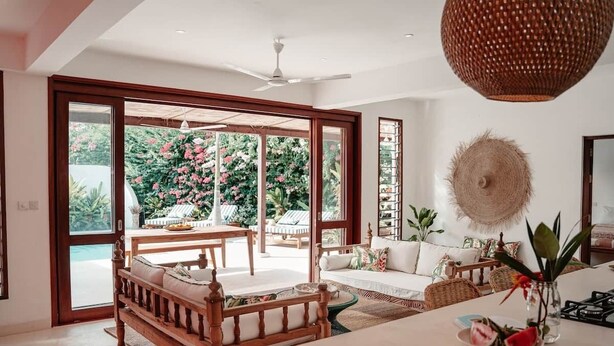 Un vaste espace de vie comprenant une grande porte-fenêtre coulissante donnant sur un balcon, un ventilateur de plafond et une table à manger avec des chaises.