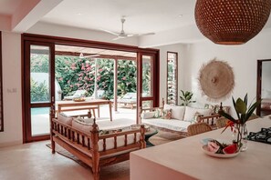 Un vaste espace de vie comprenant une grande porte-fenêtre coulissante donnant sur un balcon, un ventilateur de plafond et une table à manger avec des chaises.