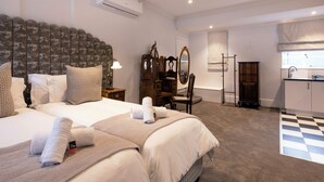 A hotel room with a large bed, a wooden headboard, a desk with a chair, a mirror, a wardrobe, and a bathroom with a checkered floor. - The Cape Town Club (Cape Town)